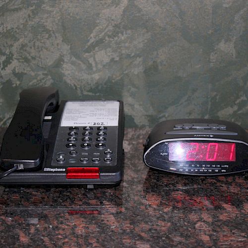 A corded telephone with a red button sits on a counter next to a digital alarm clock displaying the time 4:01.