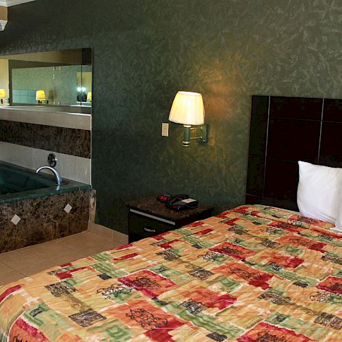 The image shows a hotel room with a bed, lamp, phone on a nightstand, and a hot tub with towels nearby. The wall behind the bed is dark green.