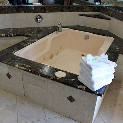 The image shows a luxurious bathtub with a dark marble surround and a stack of white towels on the edge.