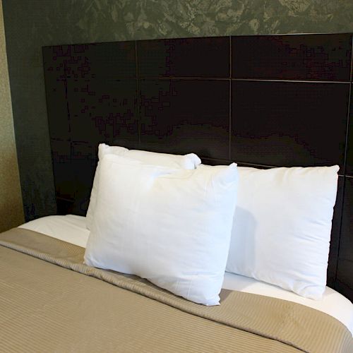 A neatly made bed with two white pillows, a beige blanket, and a dark, geometric-patterned headboard against a textured wall.