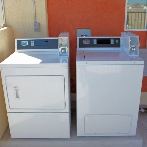 The image shows two white commercial coin-operated laundry machines placed side by side outdoors.