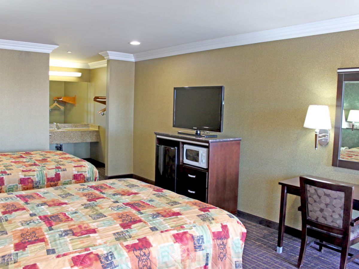 A hotel room with two beds, a TV, a desk with a chair, and a sink area near the entrance, featuring modern decor and lighting.