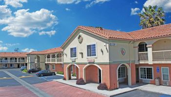 A two-story hotel with a red-tiled roof, multiple balconies, parking spaces, and clear blue skies in the background.