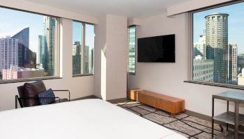 This image shows a modern hotel room with city views, featuring large windows, a wall-mounted TV, and contemporary furniture, ending the sentence.