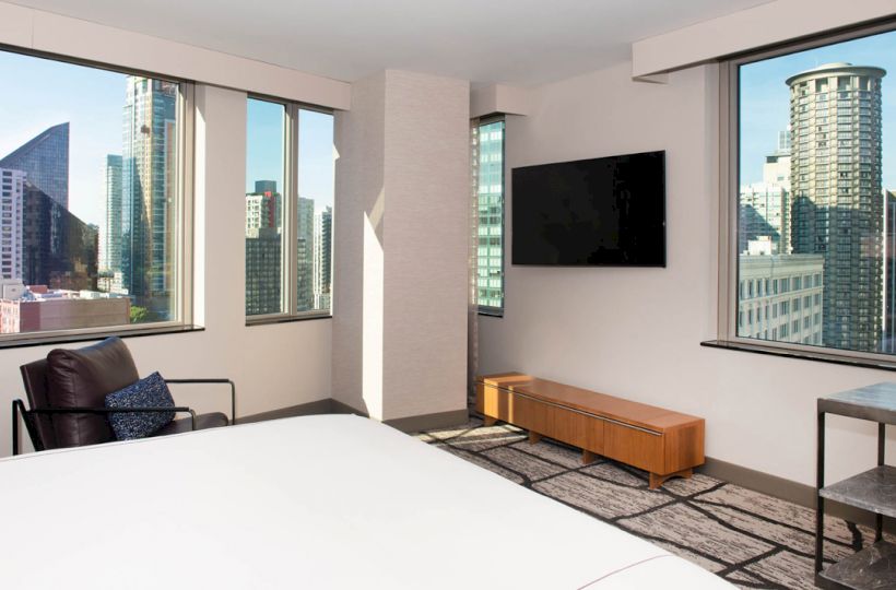This image shows a modern hotel room with city views, featuring large windows, a wall-mounted TV, and contemporary furniture, ending the sentence.