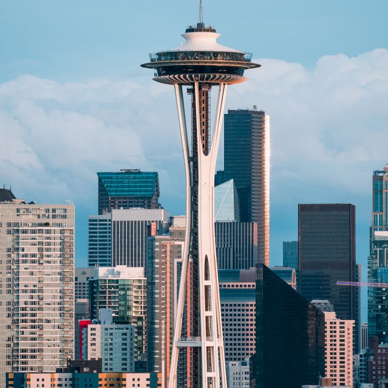 The image features the iconic Space Needle tower in Seattle, with a backdrop of modern skyscrapers and a partly cloudy sky.