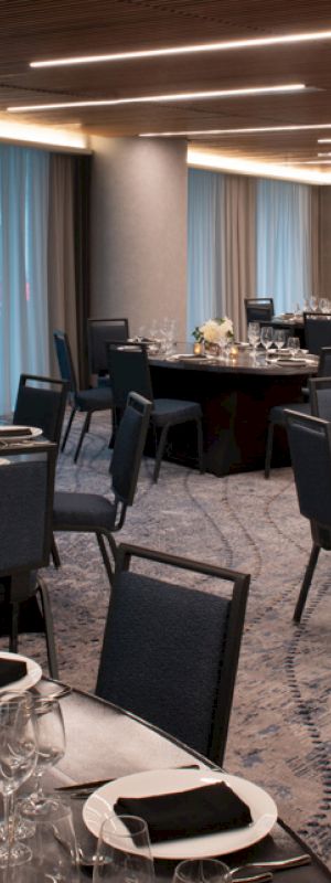 A modern banquet hall set up with round tables and chairs, adorned with elegant table settings, floral centerpieces, and blue drapes.