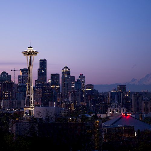 The image shows the Seattle skyline at dusk, featuring the Space Needle, downtown buildings, and Mount Rainier in the background.