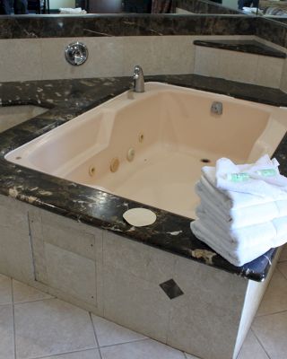 The image shows a luxurious bathtub with a granite surround, tiled flooring, and a stack of white towels placed on the edge.